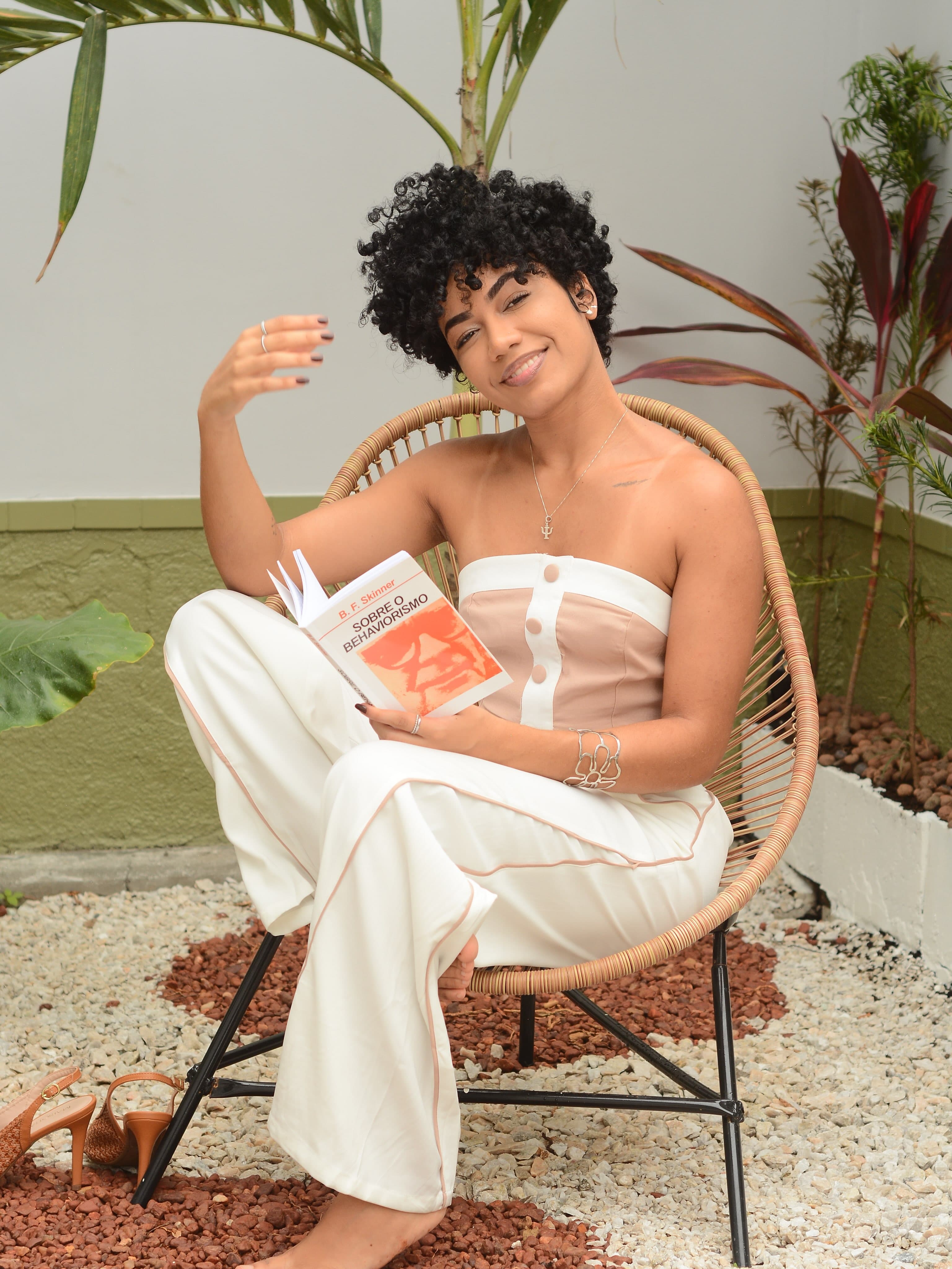 Iasmin Portugal sentada ao ar livre com um livro sobre behaviorismo